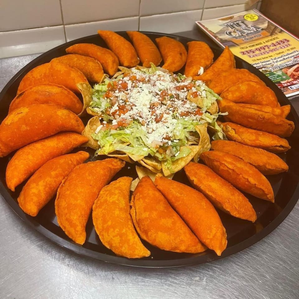 A platter of golden-orange empanadas surrounds a taco salad with lettuce, tomato, and cheese.