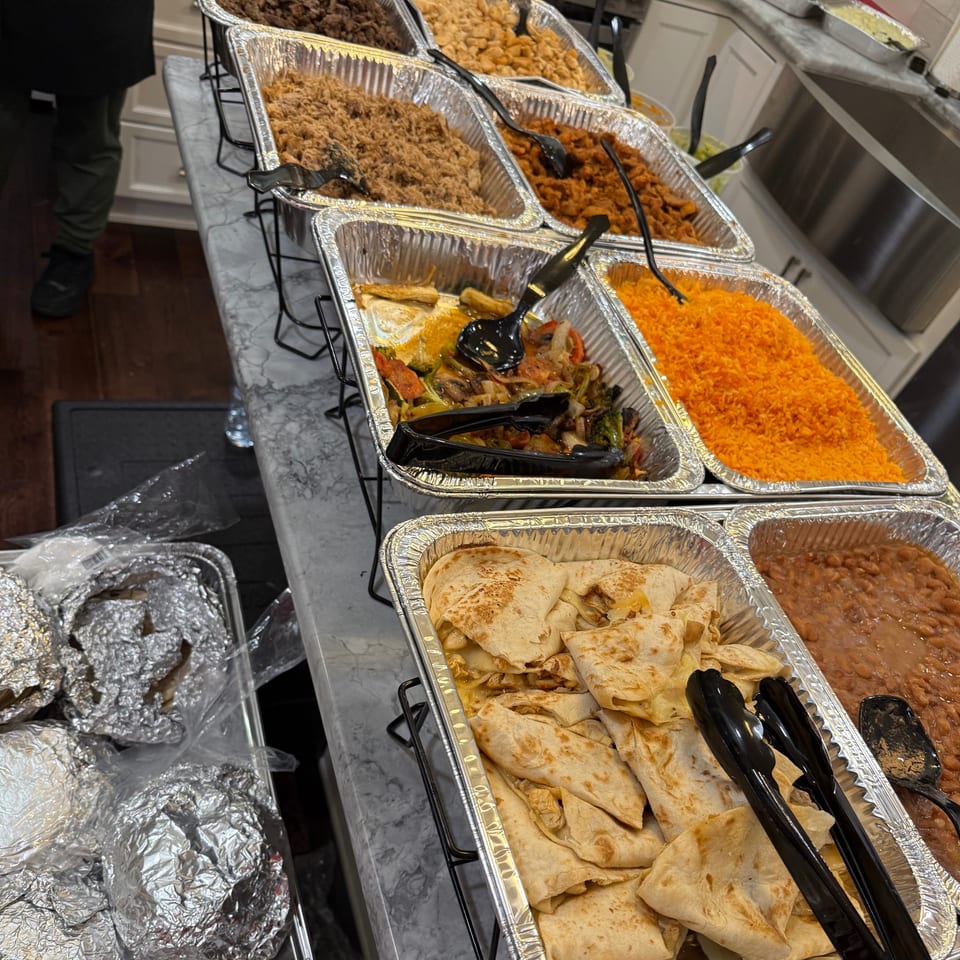 Buffet line with foil pans of various foods, including rice, beans, quesadillas, and vegetables.