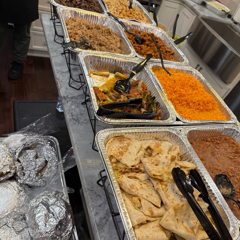 Buffet line with foil pans of various foods, including rice, beans, quesadillas, and vegetables.